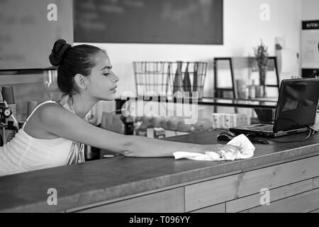 Sauber wischen. Frau Barista im Coffee Shop. Barista sauber Zähler nach oben in bar an. Pretty Woman stehen hinter cafe Zähler. Adorable junge Barkeeper oder Bar Stockfoto