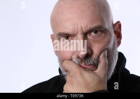 Älterer, Reifer Mann, Nachdenkliches Denken. Glatzkopf im Rentenalter mit der Hand im Gesicht. Durchstechend braune Augen auf weißem Hintergrund mit schwarzem Pullover. Stockfoto
