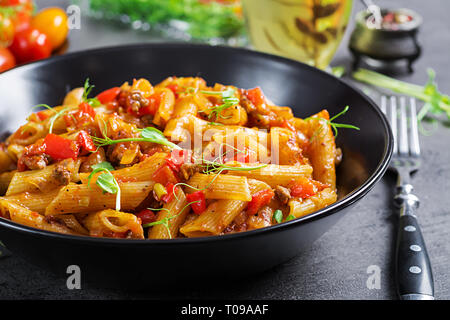 Penne Pasta in Tomatensauce mit Fleisch, Tomaten mit Erbse Sprößlinge auf einen dunklen Tisch eingerichtet. Stockfoto