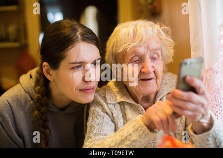 Ältere Frau sieht aus, und geben Sie auf einem Smartphone, mit seiner erwachsenen Tochter Enkelin. Stockfoto