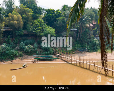 Bambus Zuckerrohr Brücke über den Fluss Nam Kahn Nebenarm des Mekong mit traditionellen überdachten Einbaum Flussschiff, Luang Prabang, Laos, Indochina, Se Asien Stockfoto