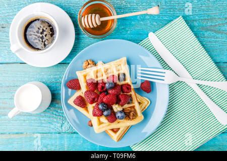Selbstgemachte Waffeln mit Himbeeren und Blaubeeren, Tasse Kaffee, Milch und Besteck Stockfoto