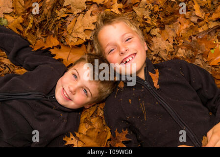 KWO Kinder legen in einem Haufen von Blättern Stockfoto