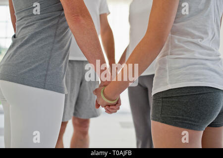 Gruppe von Menschen in einem Kreis stehen und halten sich an den Händen während einer Yogastunde. Stockfoto