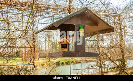 Ökologische Kombination aus einem Bird Feeder und ein Hotel für Insekten hängen von einem Baum mit einem Teich im Hintergrund, wunderschönen und sonnigen Wintertag Stockfoto