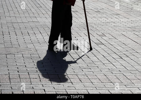 Silhouette der Altstadt von Person zu Fuß mit einem Stock, lange Schatten auf Pflaster. Konzept für Erwerbsunfähigkeit, Alter, hinkt oder blind, Erkrankungen der Wirbelsäule Stockfoto