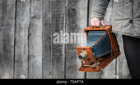 Large Format retro Kamera in Fotograf Hand. Konzept - Fotografie der 1930er Jahre 1950er Jahre. Retro Holz- Wand im Hintergrund, kopieren Platz für Text Stockfoto