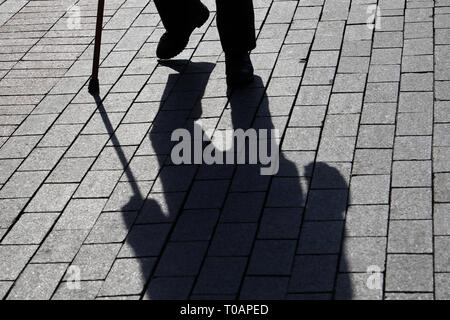 Silhouette der Mann mit einem Stock, lange Schatten auf Pflaster. Konzept der hinkt oder blind Person, Invalidität, Alter, Armut, Krankheiten der Wirbelsäule Stockfoto