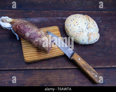 Eine iberische Schwein Wurst auf einem alten Holzplatte mit einem antiken Messer und ein Laib Brot Spanisch rustikalen Saatgut Stockfoto