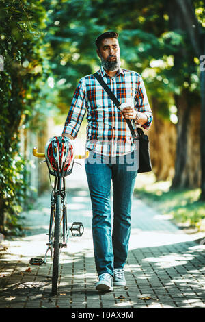 Ein hübscher junger Mann geht in die Stadt fahren mit dem Fahrrad, Wandern mit Kaffee daneben und zu überlegen, wo er gehen würde. Stockfoto