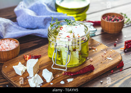 Feta Käse, mariniert in Olivenöl mit frischen Kräutern in Glas. Holz- Hintergrund. Stockfoto