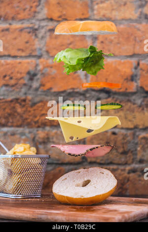 Bagel Sandwich Floating Levitation fallende Zutaten. Frisch und lecker Sandwich magisch. Rustic weiß/roten Ziegelwand Hintergrund. Chips/Jetons Stockfoto