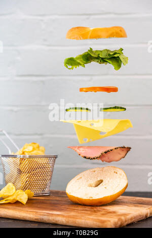 Bagel Sandwich Floating Levitation fallende Zutaten. Frisch und lecker Sandwich magisch. Rustic weiß/roten Ziegelwand Hintergrund. Chips/Jetons Stockfoto