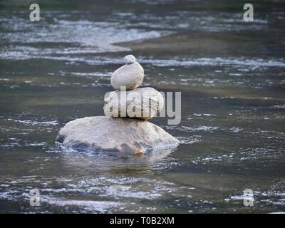 Stapel von Steinen prekär auf einem größeren Stein im Fluss ausgeglichen Stockfoto