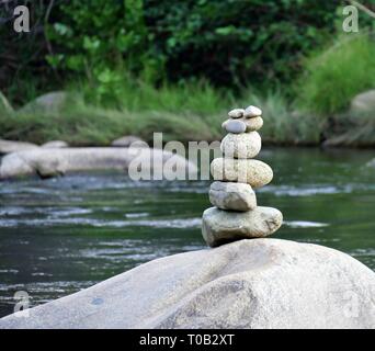 Stapel von Steinen prekär auf einem Felsen im Fluss ausgeglichen Stockfoto