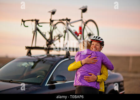 Lächelnde junge Frauen teilen sich eine liebevolle Umarmung, wie Sie sich vorbereiten: Nach einem langen Tag Radfahren. Stockfoto