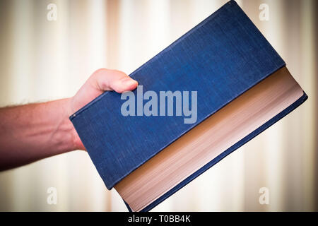 Große schwere blaue Buch in der Hand; Übergabe an (oder das Buch jemand zu werfen). Stockfoto