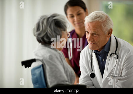 Arzt und Krankenschwester sprechen zu einem älteren Patienten im Rollstuhl. Stockfoto