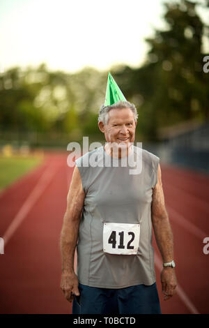 Porträt eines lächelnden älteren Mann, der eine Partei hatte auf der Leichtathletikbahn. Stockfoto