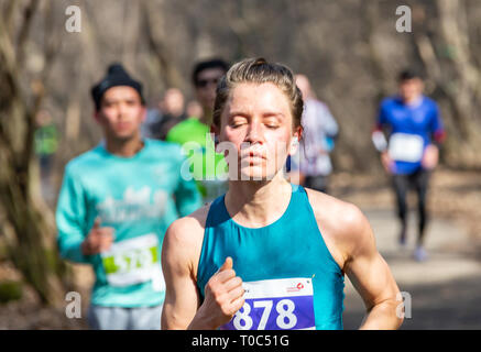 ALMATY, Kasachstan - 16. MÄRZ 2019: eine dichte Gruppe von unbekannten Männern und Frauen läuft durch ein Wäldchen im Frühjahr Marathon in der Stadt Almaty, Stockfoto