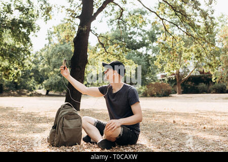 Ein junger Kerl oder Student mit einem Mobiltelefon über Video oder Musik und Video in einem Herbst Park. Stockfoto