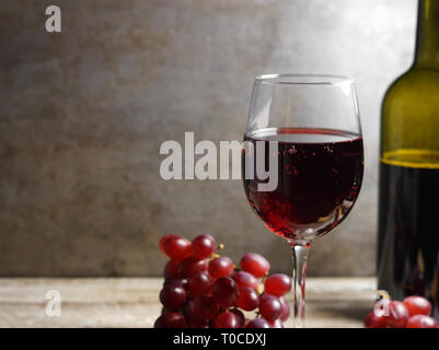 Glas Rotwein auf einem hölzernen Tisch in einem rustikalen und Vintage Wine Bar mit Trauben, Obst und eine Flasche Wein auf dem Hintergrund Detailansicht. Stockfoto