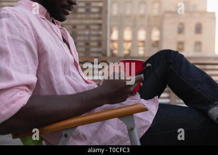 Mann mit Handy während des kalten Drink auf dem Balkon zu Hause Stockfoto