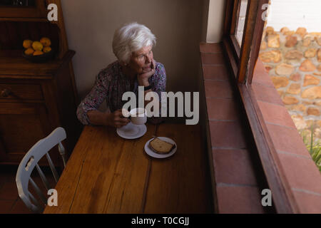 Nachdenklich Active Senior Frau suchen durch das Fenster beim Kaffee in der Küche zu Hause. Stockfoto