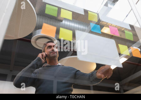 Unternehmer Gespräch am Handy während Haftnotizen suchen Stockfoto