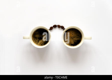 Homan Gesicht mit Brille aus zwei Espresso Tassen und Kaffeebohnen. Kaffee Kunst oder kreatives Konzept. Ansicht von oben Stockfoto