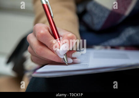 Ein Bild von einer Hand und Stift ausfüllen eines Formulars. Frau Hände mit Pastell Maniküre mit Pen. Die Beschäftigung. Unterzeichnung des Dokuments Stockfoto