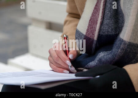 Ein Bild von einer Hand und Stift ausfüllen eines Formulars. Frau Hände mit Pastell Maniküre mit Pen. Die Beschäftigung. Unterzeichnung des Dokuments Stockfoto