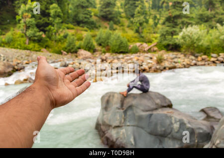 Eine Person auf eine andere Person sitzt neben einem schnell fließenden Bach in Pahalgam in Kaschmir winken Stockfoto