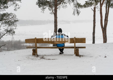 Mann sitzt auf der Bank in der Schneesturm, der die Ansicht Stockfoto