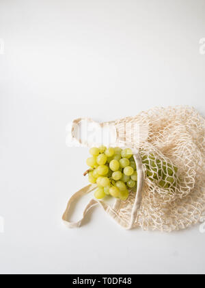 Umweltfreundliche beige Einkaufstasche mit Trauben auf einem weißen Hintergrund. String Beutel mit Früchten. Null Abfall, kein Plastik Konzept. Platz kopieren Stockfoto