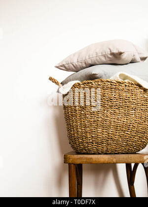 Weidenkorb mit Kissen grau auf einer hölzernen vintage Stuhl gegen eine weiße Wand. Platz kopieren Stockfoto