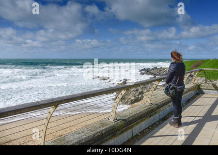 Eine Frau allein stehend an einem windigen Tag auf einem Balkon mit Blick auf den Fistral Beach in Newquay in Cornwall. Stockfoto