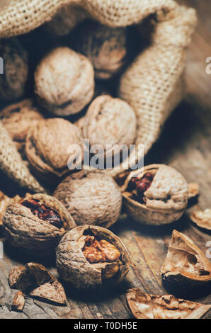 Stillleben mit Walnüssen und rissig Muscheln im Vintage sackleinen Tasche. Ganze walnut Kernels und kurz auf rustikalen Holztisch Hintergrund. Stockfoto