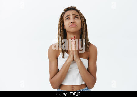 Düstere verzweifelten afrikanischen amerikanischen Mädchen mit Dreadlocks beten Gott Hände halten in Beten runzelte die Stirn, unglücklich Grimasse, mit traurigen Elend Stockfoto