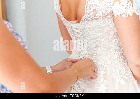 Brautjunfer Vorbereitung der Braut für die Hochzeit. Brautjunfer helfen Braut befestigen Sie Ihre Hochzeit weiß Kleid mit Schnürung vor der Zeremonie. Luxus Brautkleid schließen Stockfoto