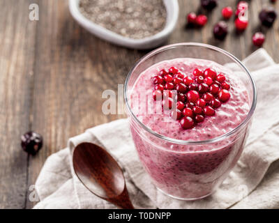 Idee für gesundes Frühstück am Valentinstag: Rosa chia Pudding mit roten Beeren pürieren und Preiselbeeren in Form von Herzen auf der Oberseite über holztisch Hintergrund. Kopieren Sie Platz für Text Stockfoto
