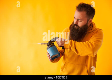 Bärtige handy man Holding Brenner auf gelben Hintergrund. Professionelles Werkzeug. Blue Tool Stockfoto