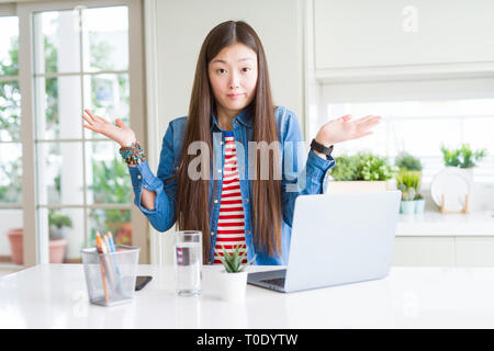 Schöne asiatische Frau mit Computer Laptop ratlos und verwirrt Ausdruck mit den Armen und hob die Hand. Zweifel Konzept. Stockfoto