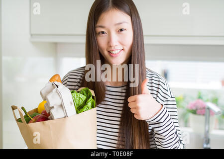 Schöne asiatische Frau mit papiertüte von frischen Lebensmitteln zufrieden mit Lächeln tun ok Zeichen, Daumen hoch, mit den Fingern, ausgezeichnete Zeichen Stockfoto