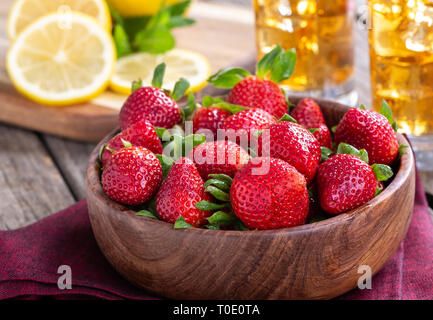 Frische Erdbeeren in eine hölzerne Schüssel mit dreinks und in Scheiben geschnittene Zitronen im Hintergrund Stockfoto