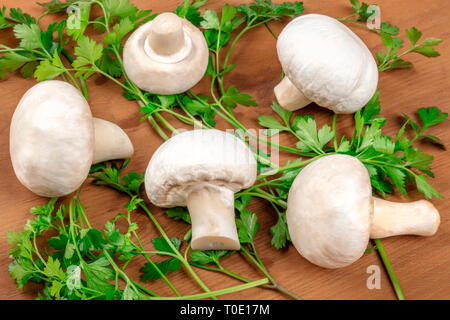 Ein Foto von champignon Pilze auf einem rustikalen Holzmöbeln Hintergrund mit frischer Petersilie Stockfoto