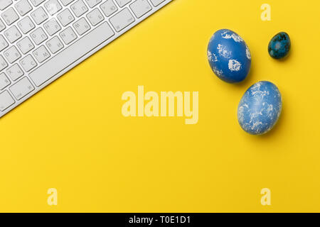 Blaue Ostereier mit Tastatur auf gelben Hintergrund. Konzept der Office Ostern. Flach, Ansicht von oben, freier Platz für Text Stockfoto