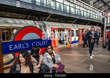 Passagiere, die auf dem Bahnsteig auf einen Zug der District Line am U-Bahnhof Earls Court in London, Großbritannien, warten Stockfoto