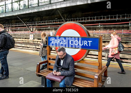 Ein Mann, der auf einer Bank in der U-Bahn-Station Earls Court, London, Großbritannien, sitzt Stockfoto
