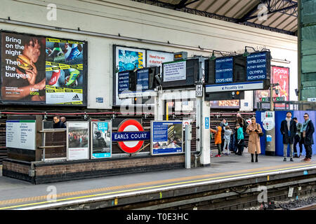 Menschen, die auf dem Bahnsteig auf einen Zug der District Line am U-Bahnhof Earls Court in London, Großbritannien, warten Stockfoto